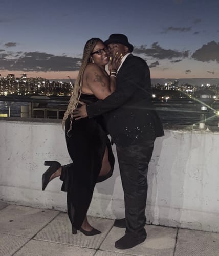 A happy reviewer and her partner embracing on a balcony overlooking a city skyline at dusk.