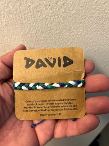 Reviewer holding the woven blue, green, and white DAVID Bracelet on its original cardboard packaging.