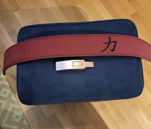 Reviewer's sturdy wine-red lever belt and its metallic buckle laid out on a cushion.