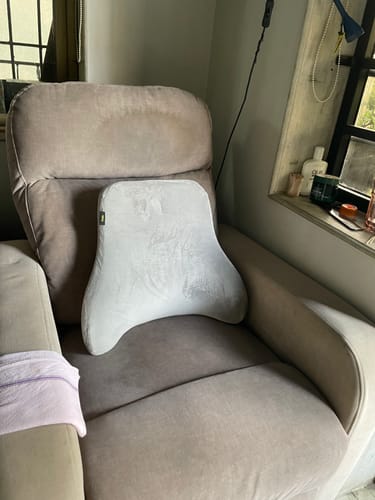 Reviewer's light-colored back support cushion placed on a plush armchair.