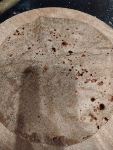 Customer's close-up of a brown roti, made from Ragi Flour, resting on a wooden board.