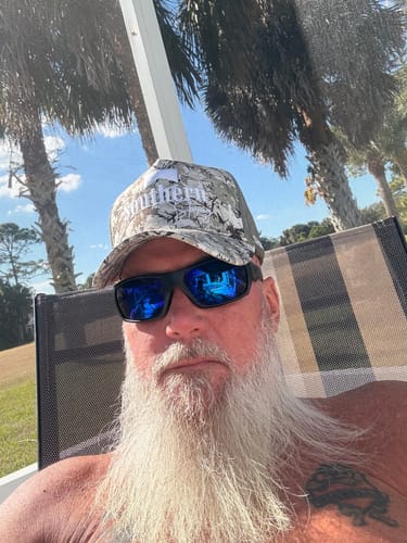 Reviewer wearing the camouflage trucker-style Hat of the Month while relaxing outdoors.
