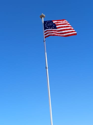 Customer's America 250 Betsy Ross Flag waving on a flagpole against a clear blue sky.