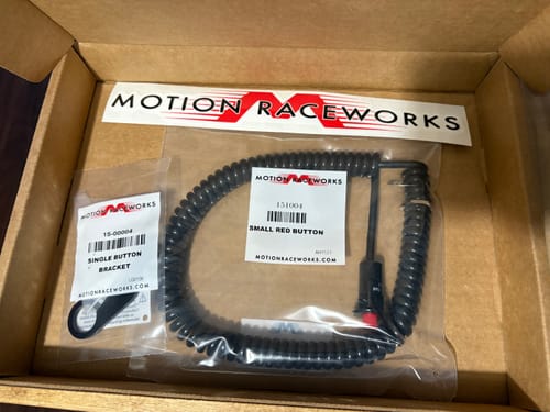Reviewer's Motion Raceworks steering wheel bracket and red push button with a coiled cord inside the box.