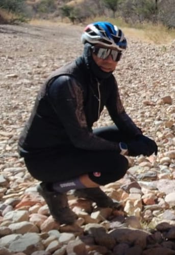 Reviewer in full cycling gear wearing dark GLIDECHIC 2.X SOCKS while crouching on a rocky trail.