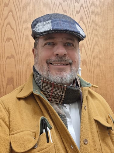 Customer smiling while wearing their patchwork Donegal Touring Cap in grey and blue tweed.