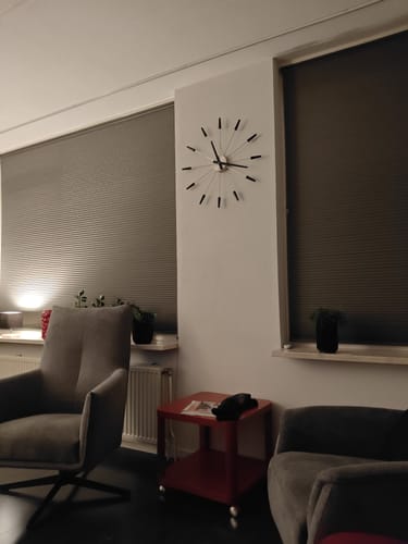 Recensent toont de moderne NeXtime Plug Inn Wandklok hangend aan de muur in een woonkamer.