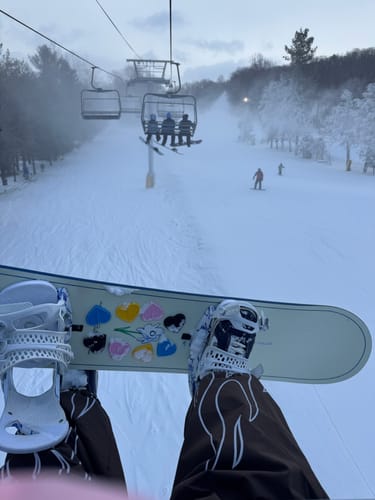 Reviewer's point-of-view from a ski lift showing the baggy fit of their dark snow pants with a white flame design.