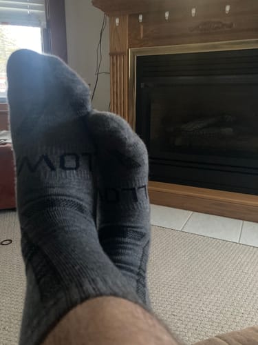 Customer relaxing indoors with feet up, wearing the gray Men's Alpaca Socks by a fireplace.