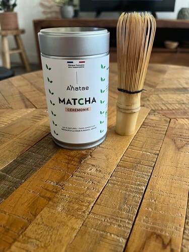 Avis du client : la boîte de Thé Matcha Cérémonie et un fouet en bambou posés sur une table.