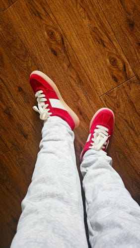 לקוח/ה נועל/ת את סניקרס Santos האדומות עם מכנסי טרנינג אפורים, במבט מלמעלה.