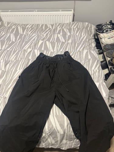 Customer's black baggy snow pants with a drawstring waist laid out flat on a bed.