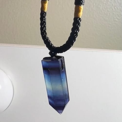 Customer's Natural Fluorite Necklace with a blue crystal pendant hanging from a black cord with gold accents.