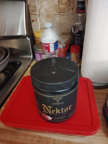 Customer's tub of Nektar supplement sitting on a red container lid on a kitchen counter.