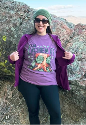 Reviewer smiling outdoors, wearing the purple 'I'm Lichen It T-shirt' under an open jacket.