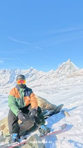 Reviewer sitting on a snowy mountain wearing the navy blue baggy snow pants.