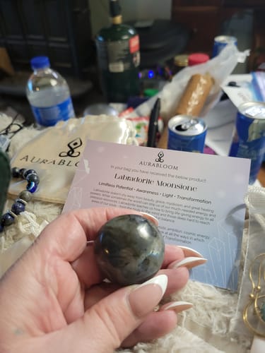 Customer holding a polished, round Labradorite Moonstone from their VIP Crystal Club box with the info card.