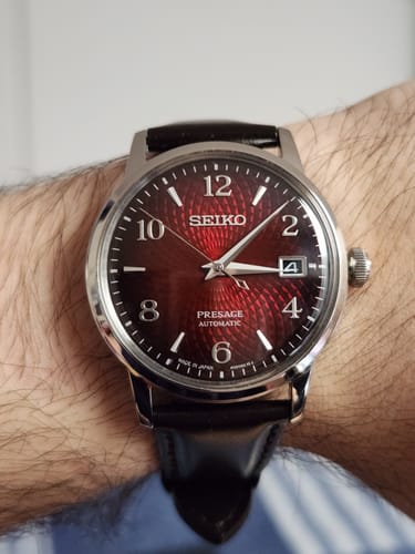 Primer plano del reloj Seiko Presage Cocktail de un cliente en su muñeca, mostrando la esfera roja texturizada.