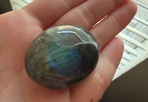 Reviewer holding their monthly crystal, a polished labradorite stone, in their palm showing its iridescent colors.