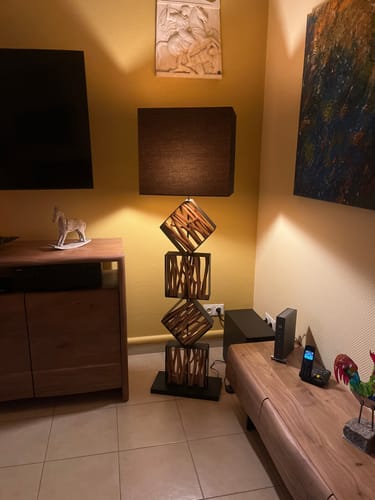 Kundenbild der beleuchteten Design Stehlampe SAWA, die in einer Wohnzimmerecke neben einem Sideboard steht.