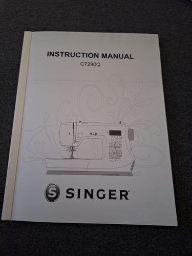 Reviewer's printed Singer C7290Q instruction manual, showing the cover of the bound book.