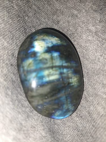 Close-up: Customer's polished Labradorite Moonstone crystal showing vibrant blue iridescence on a grey fabric.