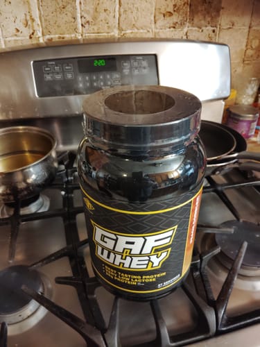 Customer's open black tub of GAF Whey protein powder sitting on a kitchen stovetop.