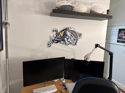 Reviewer's Naval Academy 'Jumping Goat' wall art hanging on a white wall above a desk with two computer monitors.