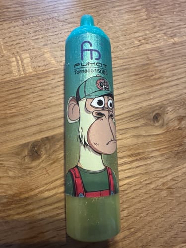 Kunde zeigt den türkisfarbenen RANDM TORNADO 15000 Vape mit Comic-Affen-Grafik auf einem Holztisch.