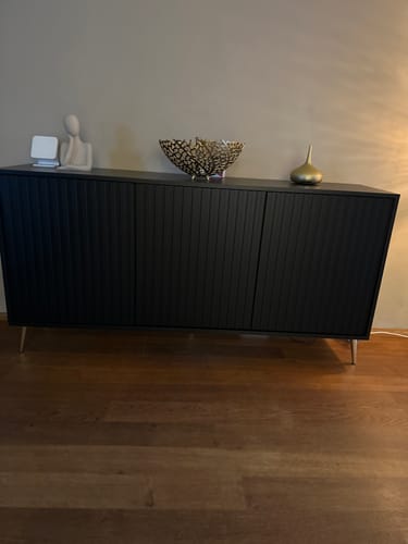 Recensent toont het zwarte Selsey Design Dressoir Giulia, opgesteld in een sfeervolle kamer.