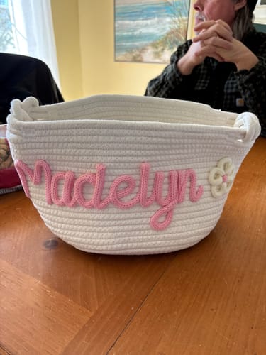 Customer's personalized knitted basket showing the name 'Madelyn' in pink yarn with a flower icon.