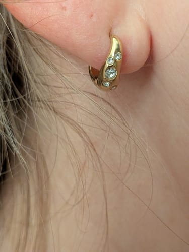 Close-up of a reviewer wearing the gold Wave Huggies with Stones on their earlobe.