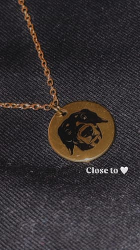 Customer's close-up of the gold Pet Portrait Necklace, showing the engraved portrait of their dog on the round pendant.