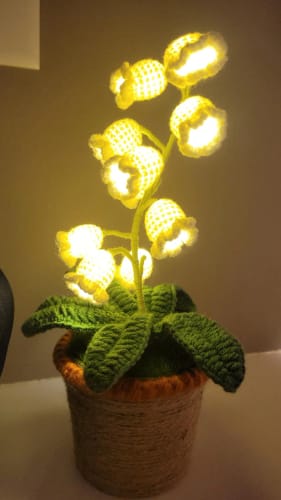 Customer's LitLamp™ Floral Crochet Lamp turned on, showing a soft, warm glow from the crocheted flowers in a rattan pot.