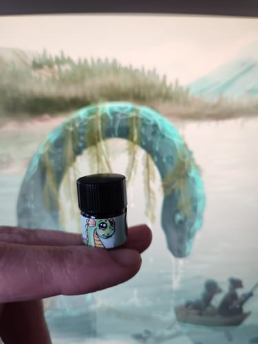 Customer holding a small vial of Nessie The Puddle Serpent in front of a matching illustration of the Loch Ness monster.