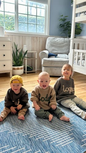 Customer's photo of three young children sitting together on a rug, wearing their oversized Hand Knitted Personalized Sweaters.