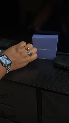 Reviewer's hand wearing the Navae Birthstone Ring with a light blue and a red stone, shown next to its box.
