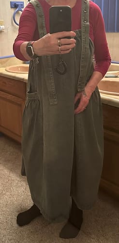Reviewer showing the loose fit of the solid denim overall dress worn over a red shirt.