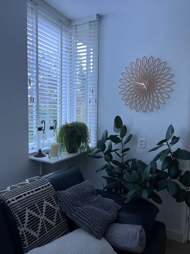 Recensent toont de sierlijke Karlsson Wandklok Sunflower die aan de muur in een woonkamer hangt.