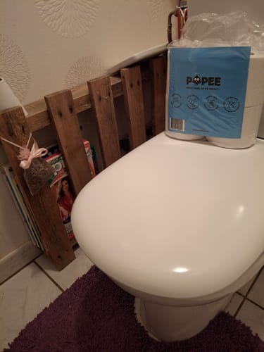 Client montrant son paquet de papier toilette compact posé sur des toilettes.