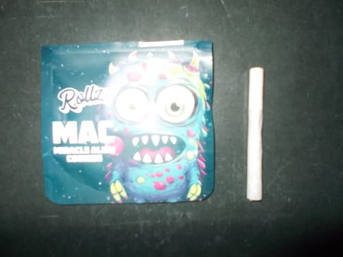 Reviewer's Miracle Alien Cookies packaging with a colorful monster graphic, shown next to a hand-rolled cigarette.