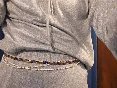 Customer wearing their Ivory Clasp Waist Beads layered with other blue and gold strands over a grey sweatsuit.