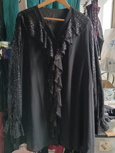 Kundens svarte bluse med paljettkledde rysjer og ermer henger på en kleshenger.