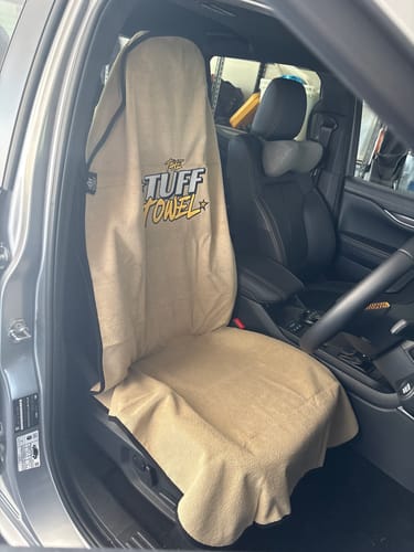 Reviewer's tan Waterproof Car Towel Seat Cover fitted over a black leather driver's seat.