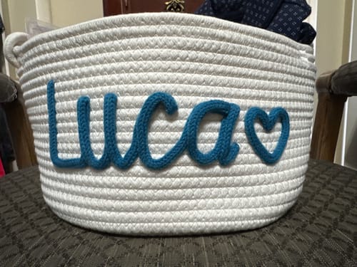 Customer's white woven basket featuring the name "Lucas" and a heart embroidered in thick teal yarn.