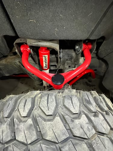 Customer's close-up of the installed red upper control arm in a vehicle's wheel well, above the tire.