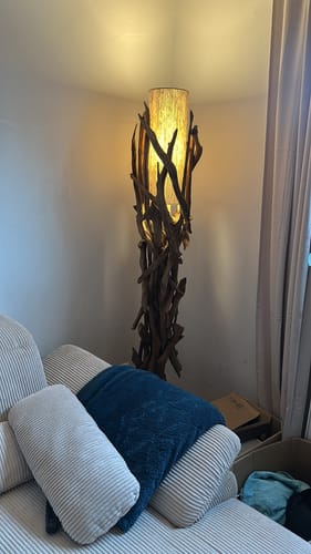 Kundenbild der beleuchteten Treibholz Stehlampe VILLA in einer Zimmerecke neben einem Sofa.
