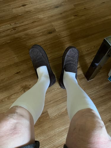Customer's legs wearing white Performance Eucalyptus Compression Socks and dark loafers against a wood floor.
