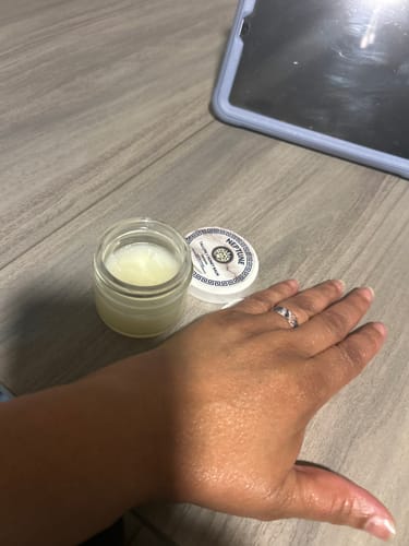 Customer's hand looking moisturized next to an open jar of Grass Fed Tallow & Honey Balm.