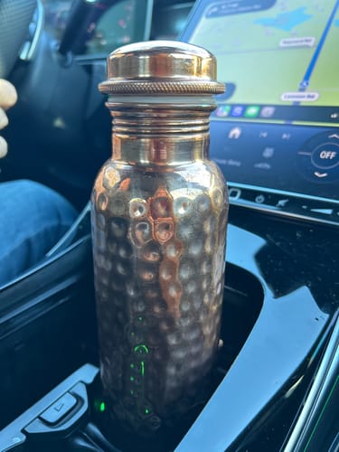 Customer's hand-hammered Pure Copper Water Bottle sitting upright in a car's center console cup holder.